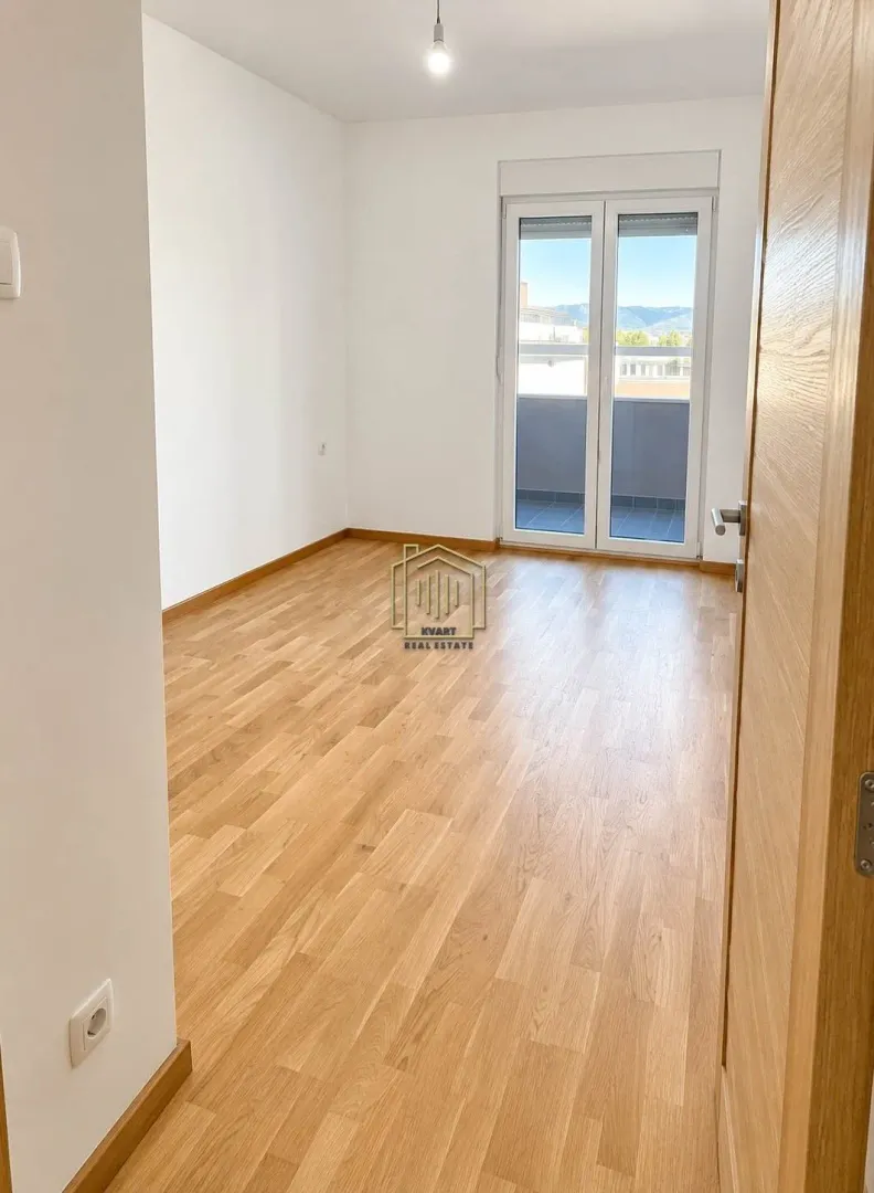 Prazna soba sa drvenim podom i balkonskim vratima.