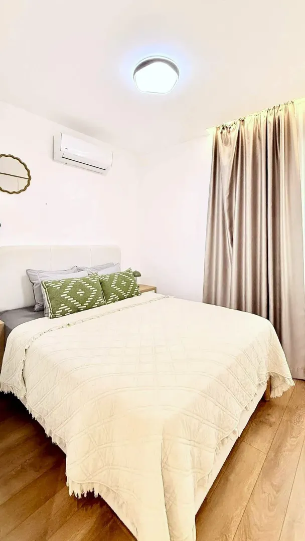 Bright bedroom with a double bed, air conditioning unit, and a window with curtains.