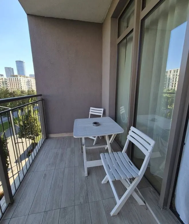 Manji namešten balkon sa garniturom za sedenje i pogledom na okolne zgrade.
