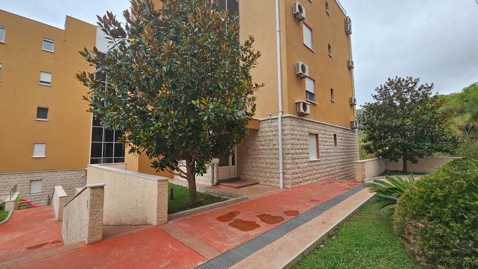 Eksterijer stambene zgrade sa uređenim dvorištem i zelenilom.