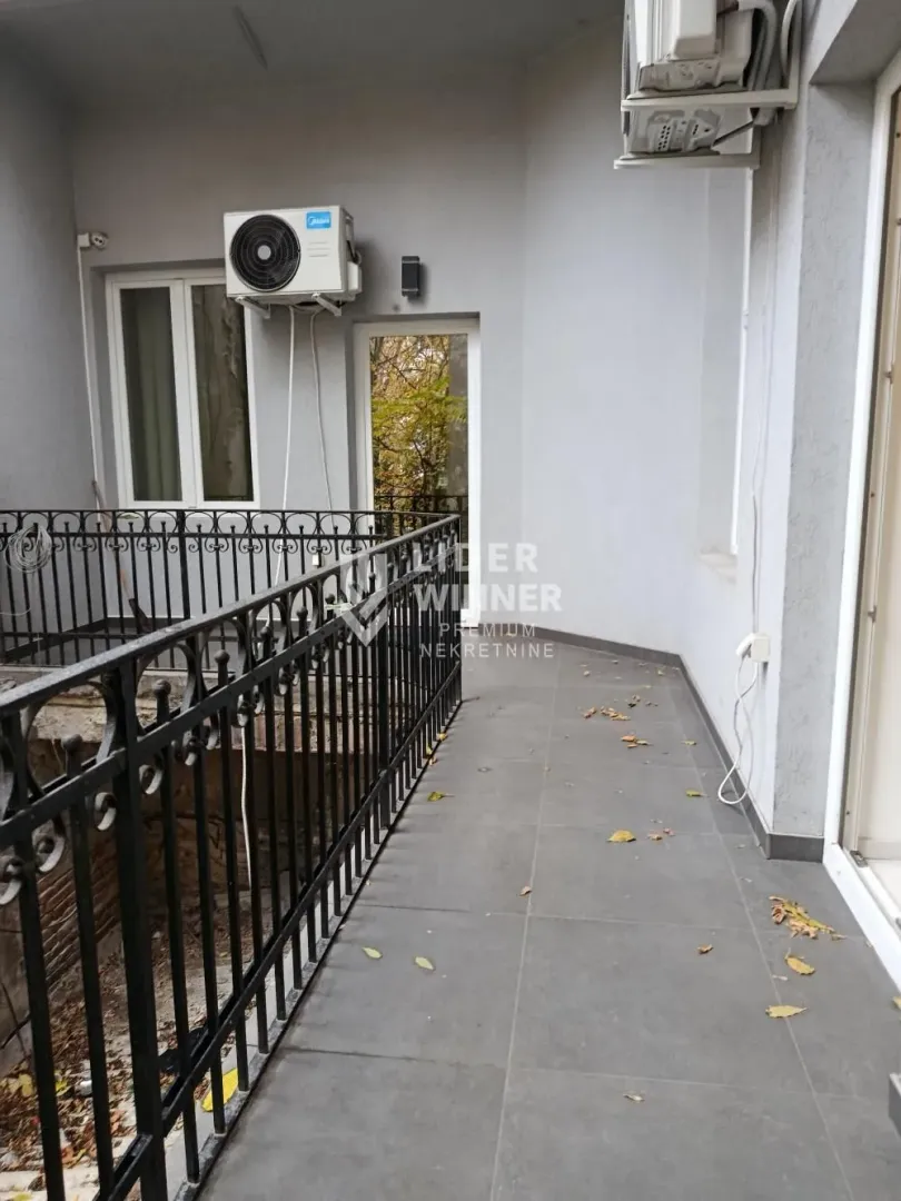 Prostrana popločana terasa sa crnom metalnom ogradom i spoljnim jedinicama klima uređaja.