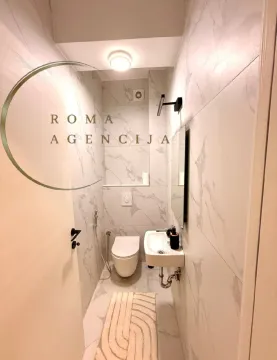 Smaller marble-tiled bathroom with a toilet and washbasin. - image 9