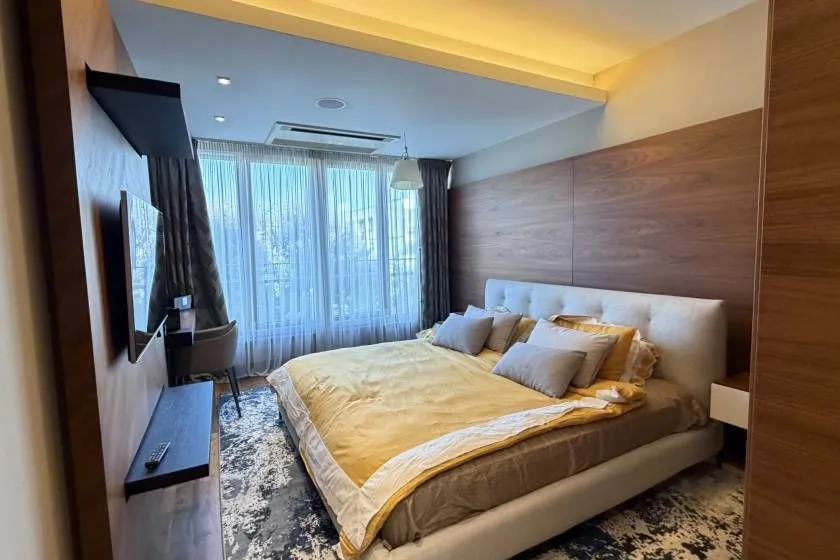 Modern bedroom with a large double bed, wooden wall panels and a large window.