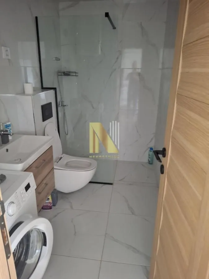 Savremeno opremljeno kupatilo sa tuš kabinom, WC šoljom, umivaonikom i mašinom za veš.