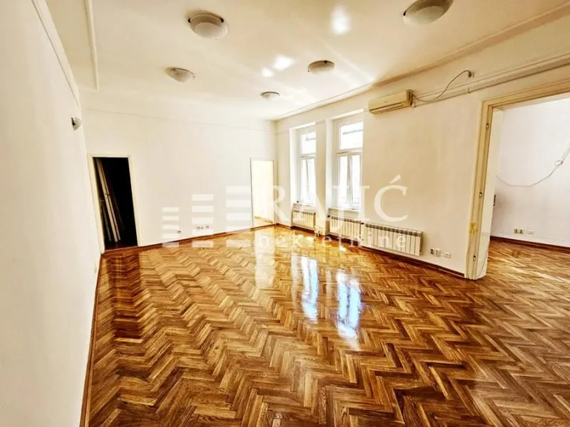 Empty spacious room with parquet flooring and white walls.
