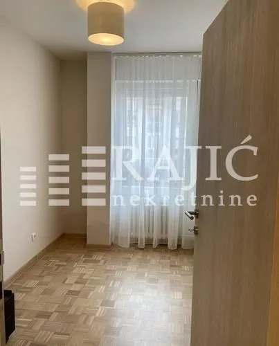 Empty room with parquet flooring and a window covered with a curtain.
