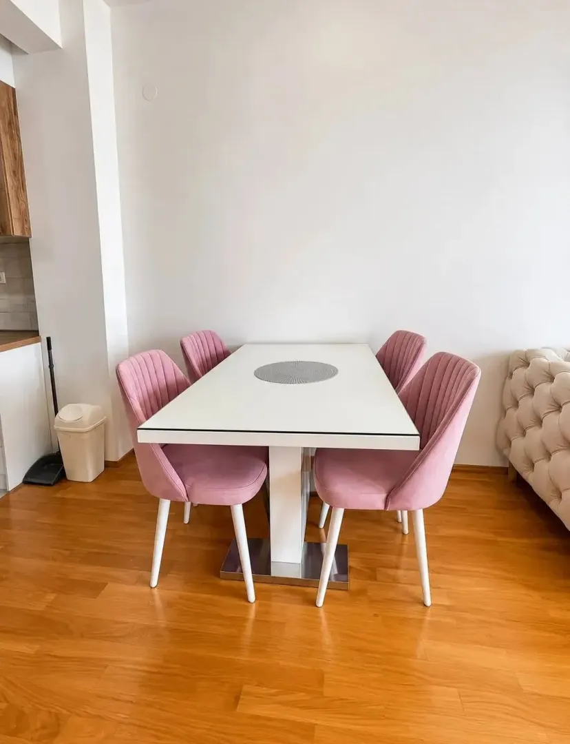 Trpezarija sa bijelim stolom i roze stolicama u stanu.