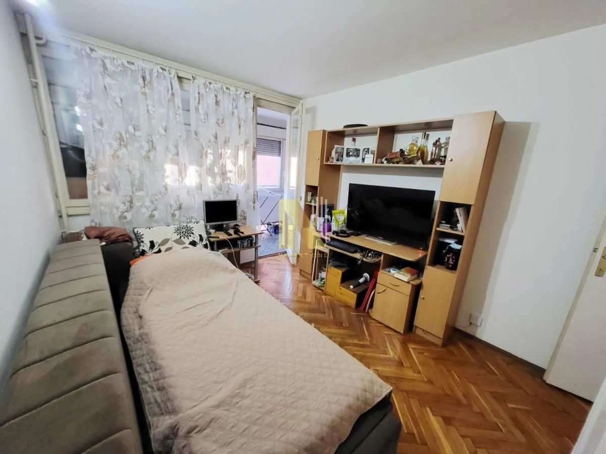 Manja spavaća soba sa krevetom, TV policom i izlazom na terasu.