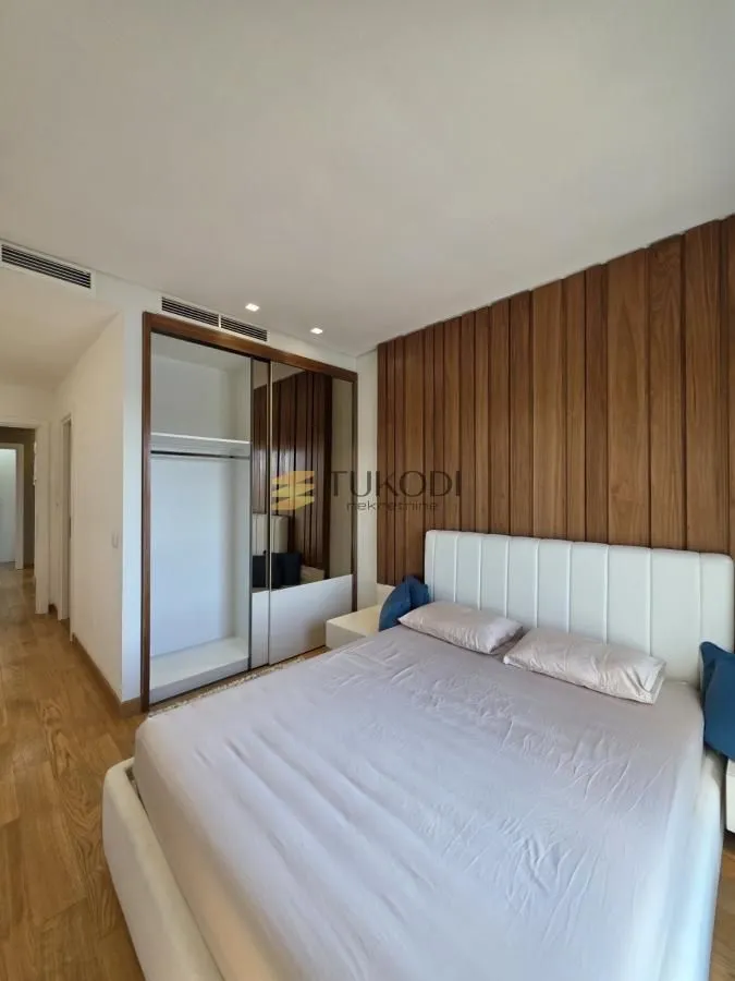 Furnished bedroom with a double bed, wooden wall paneling, and a built-in wardrobe.