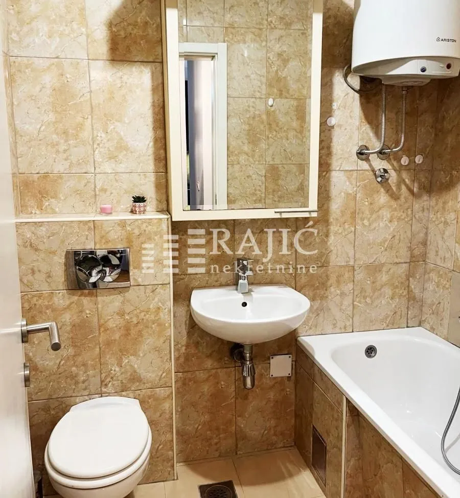 Smaller bathroom tiled with ceramic tiles featuring a bathtub, sink, and toilet.