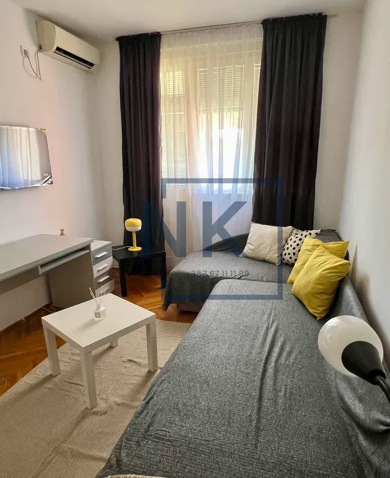 Living room with a sofa bed, desk, and a wall-mounted TV.