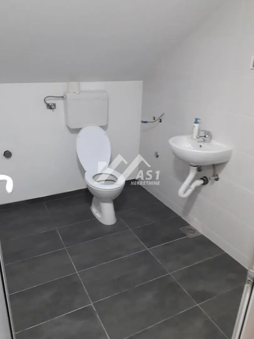 Smaller bathroom with white tiles and dark flooring under a sloped ceiling.