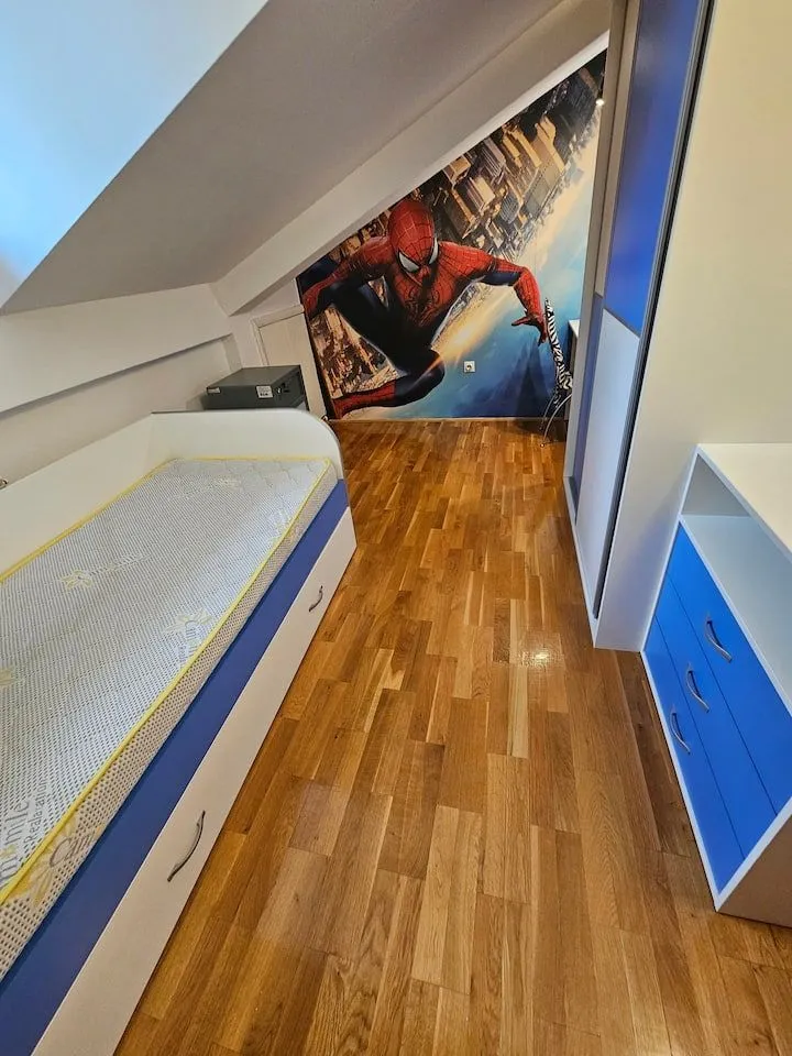 Children's attic bedroom with a bed, wardrobe, and Spiderman themed wallpaper.