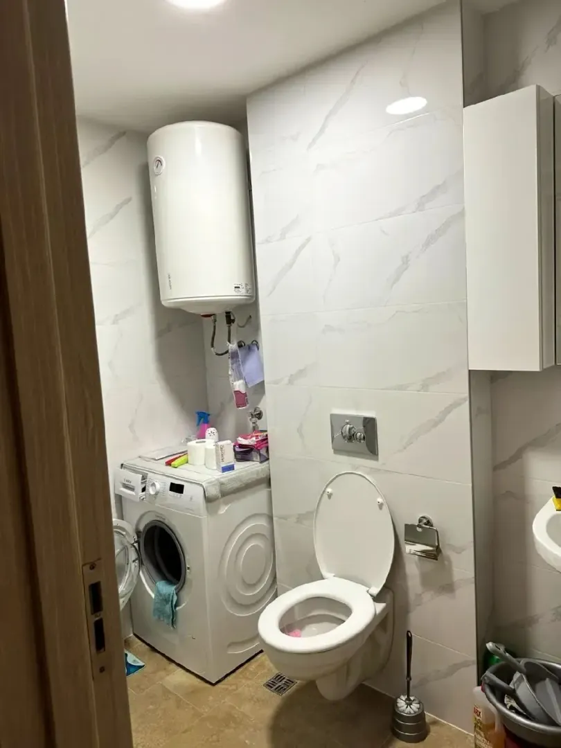 Manje kupatilo sa veš mašinom i bijelim keramičkim pločicama.