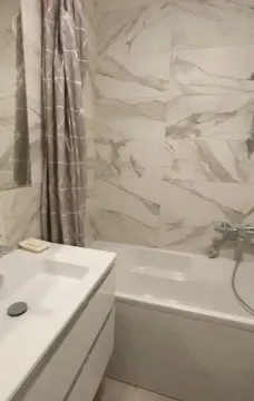 Bathroom equipped with a white washbasin, bathtub, and marble-look tiles. - image 6