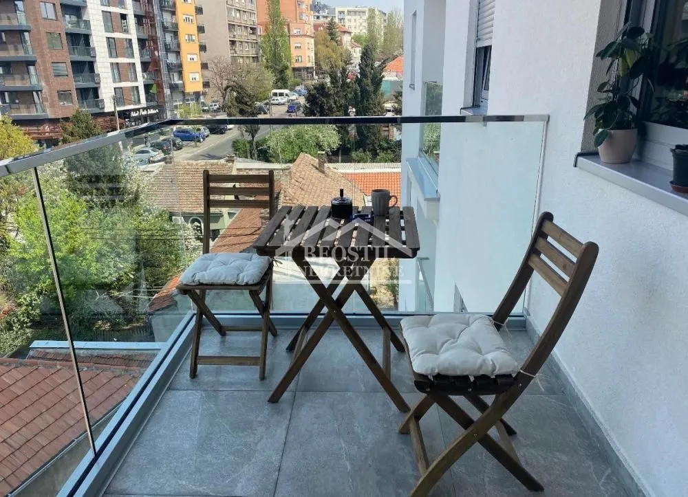 Manji namešteni balkon sa drvenim stolom i stolicama i staklenom ogradom.