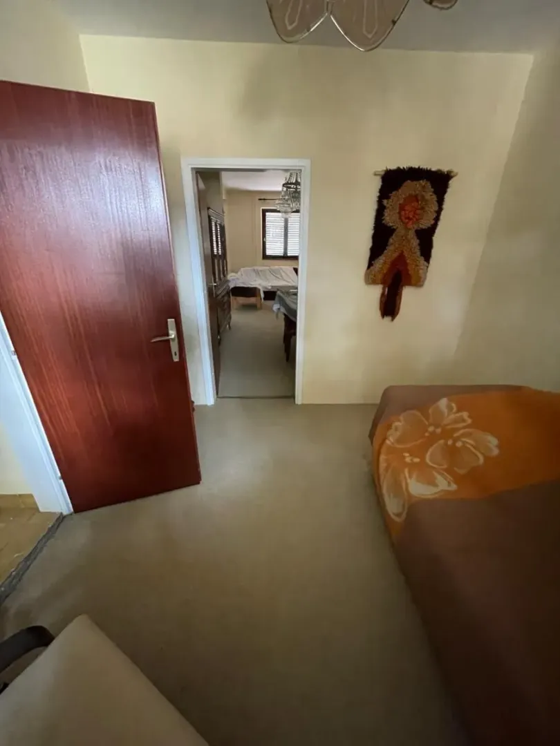 Manja spavaća soba sa krevetom i otvorenim vratima prema drugoj prostoriji.
