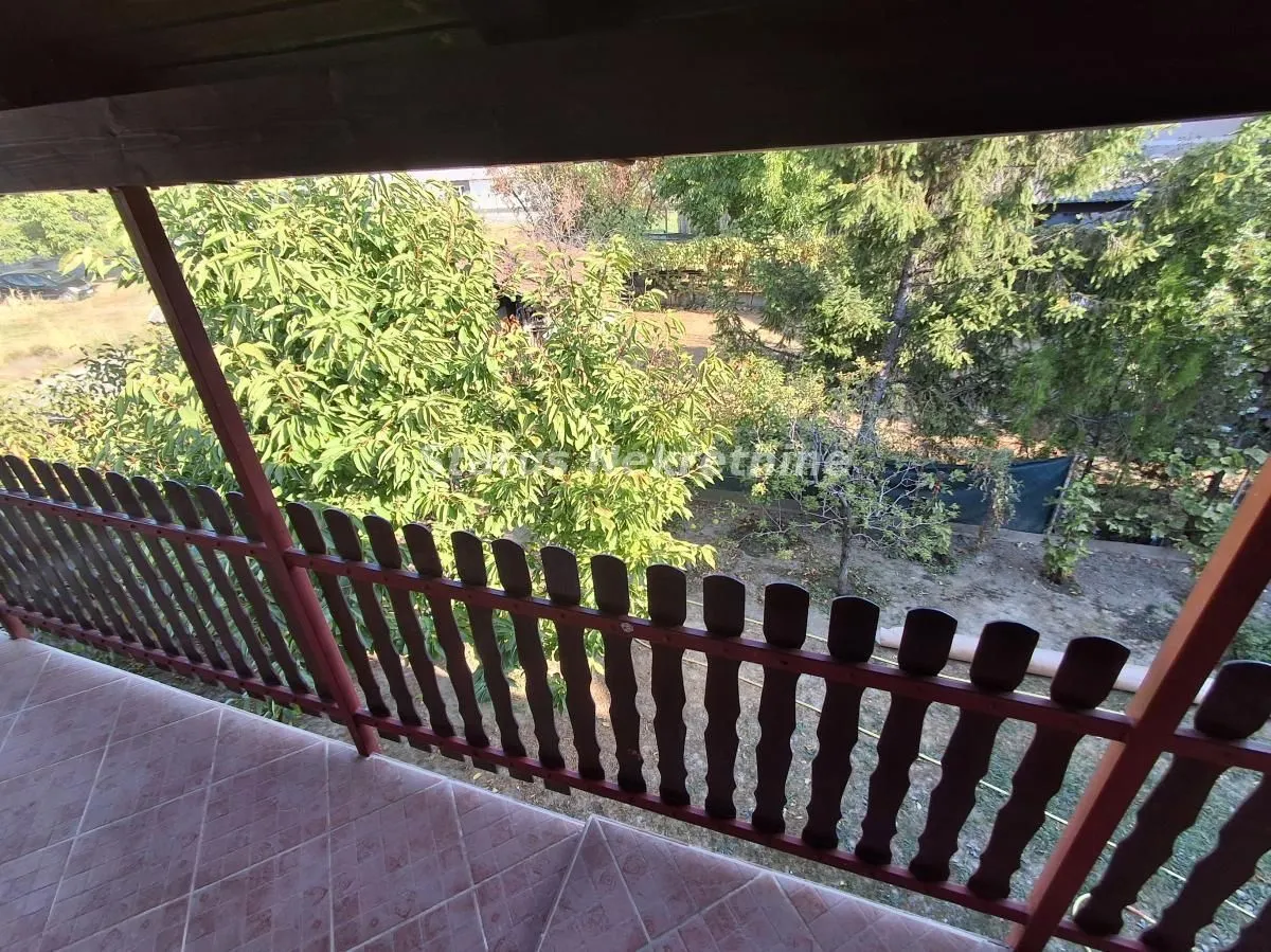 Covered balcony with a wooden railing and a view of greenery.