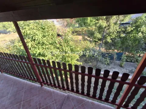 Covered balcony with a wooden railing and a view of greenery. - image 10