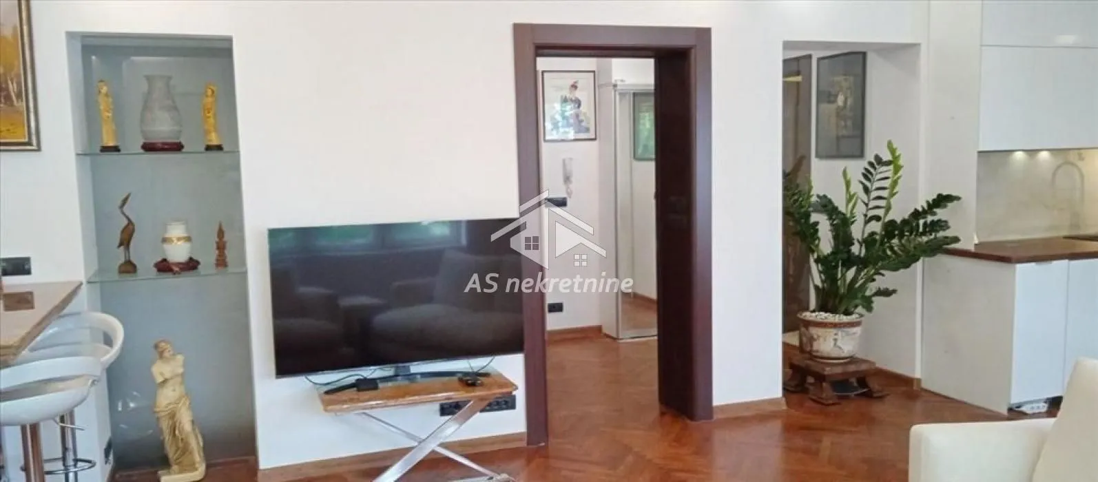 Dnevna soba sa televizorom, nišom za ukrasne predmete i parketom na podu.