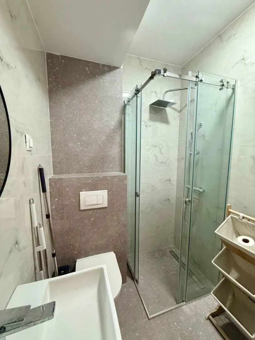 Modern bathroom with a glass shower enclosure, sink, and tiled walls.