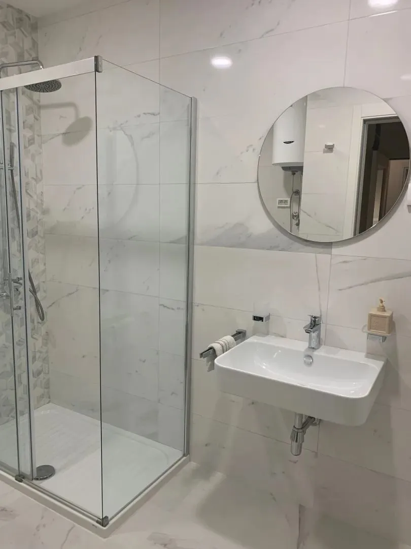 Modern bathroom with a walk-in shower, washbasin, and round mirror.