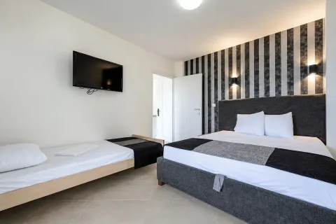 Namještena spavaća soba sa bračnim krevetom, pomoćnim ležajem i televizorom na zidu. - image 3