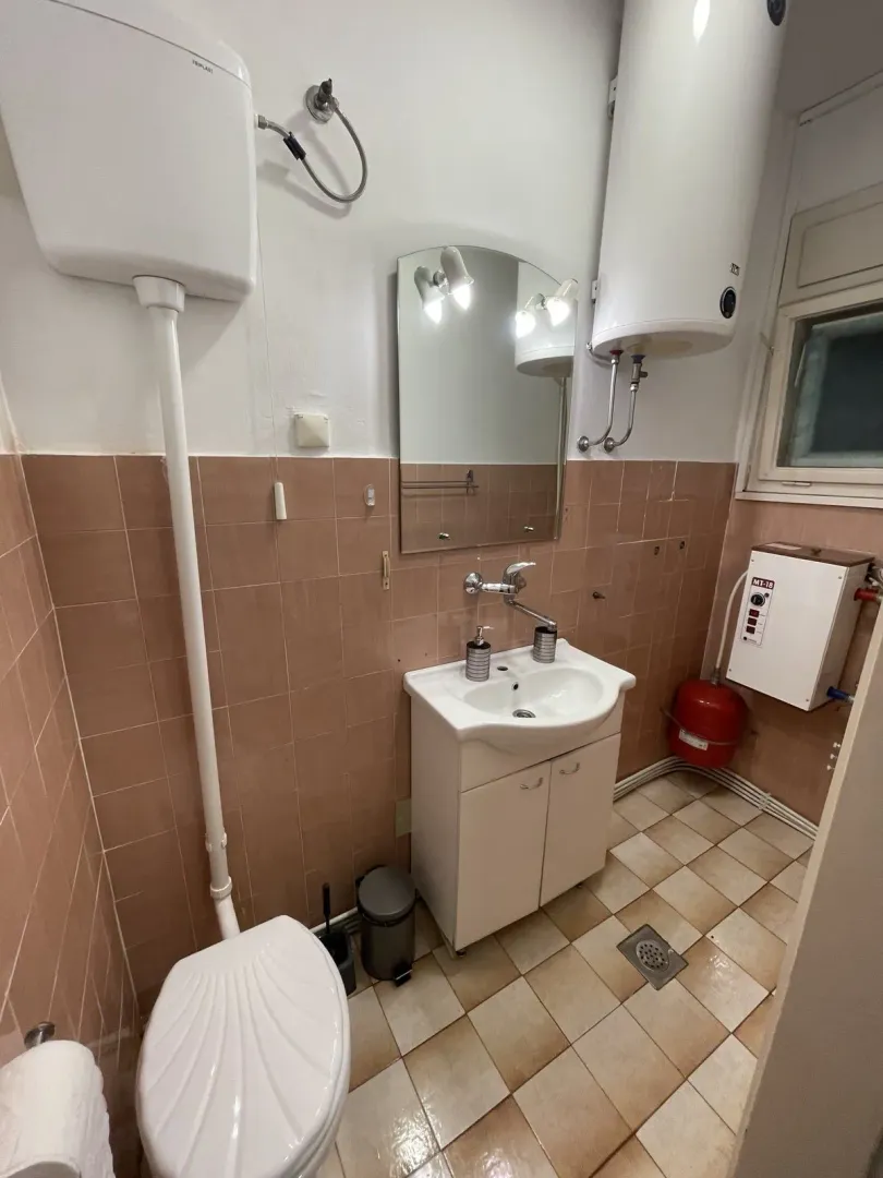 Jednostavno kupatilo sa lavaboom, ogledalom, wc šoljom i bojlerom.