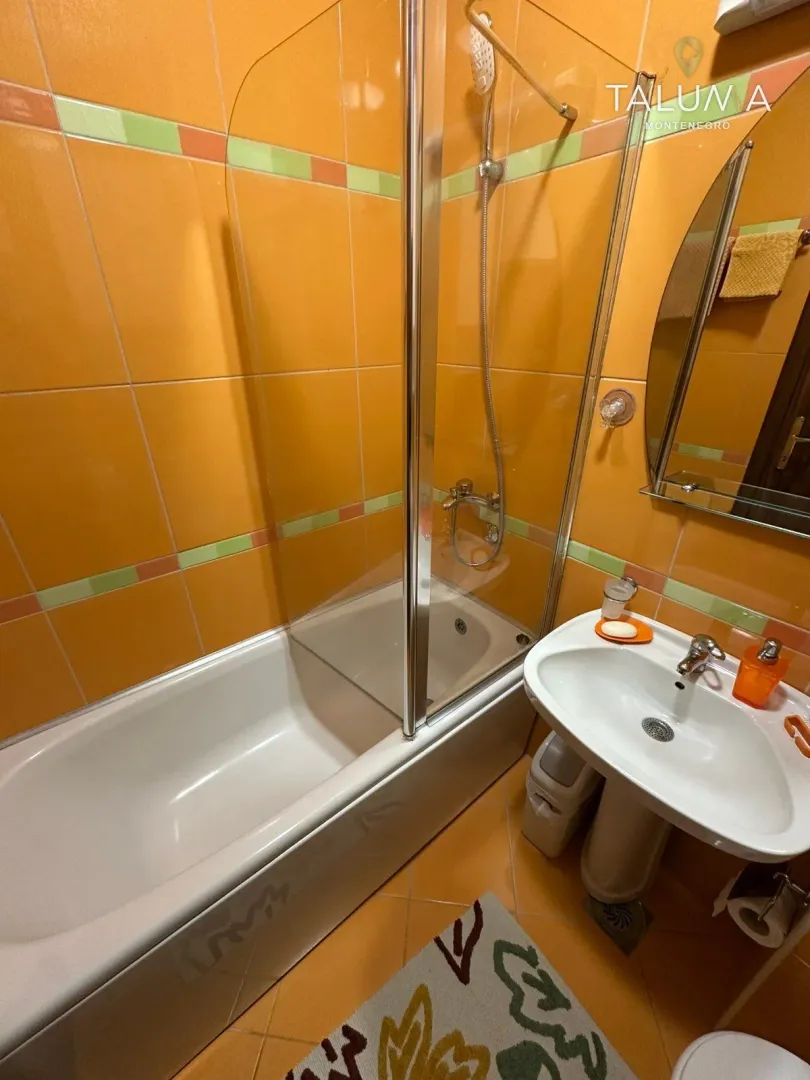 Bathroom with a bathtub, glass screen, and washbasin in orange tones.