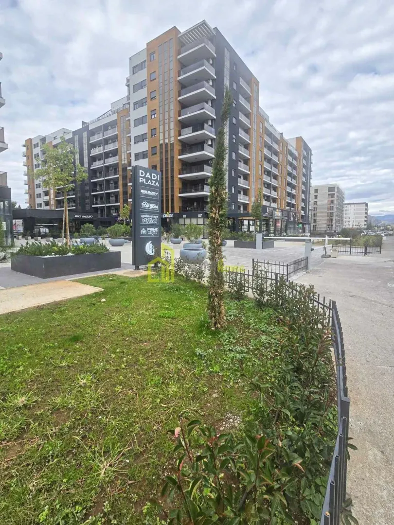 Eksterijer moderne višespratne stambene zgrade sa uređenim dvorištem i prilazom.