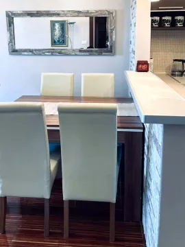 Trpezarija sa drvenim stolom i bijelim stolicama pored kuhinjskog šanka. - image 8