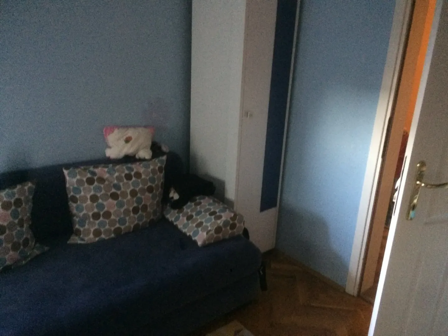 A small room featuring a blue sofa with patterned pillows and a tall wardrobe.