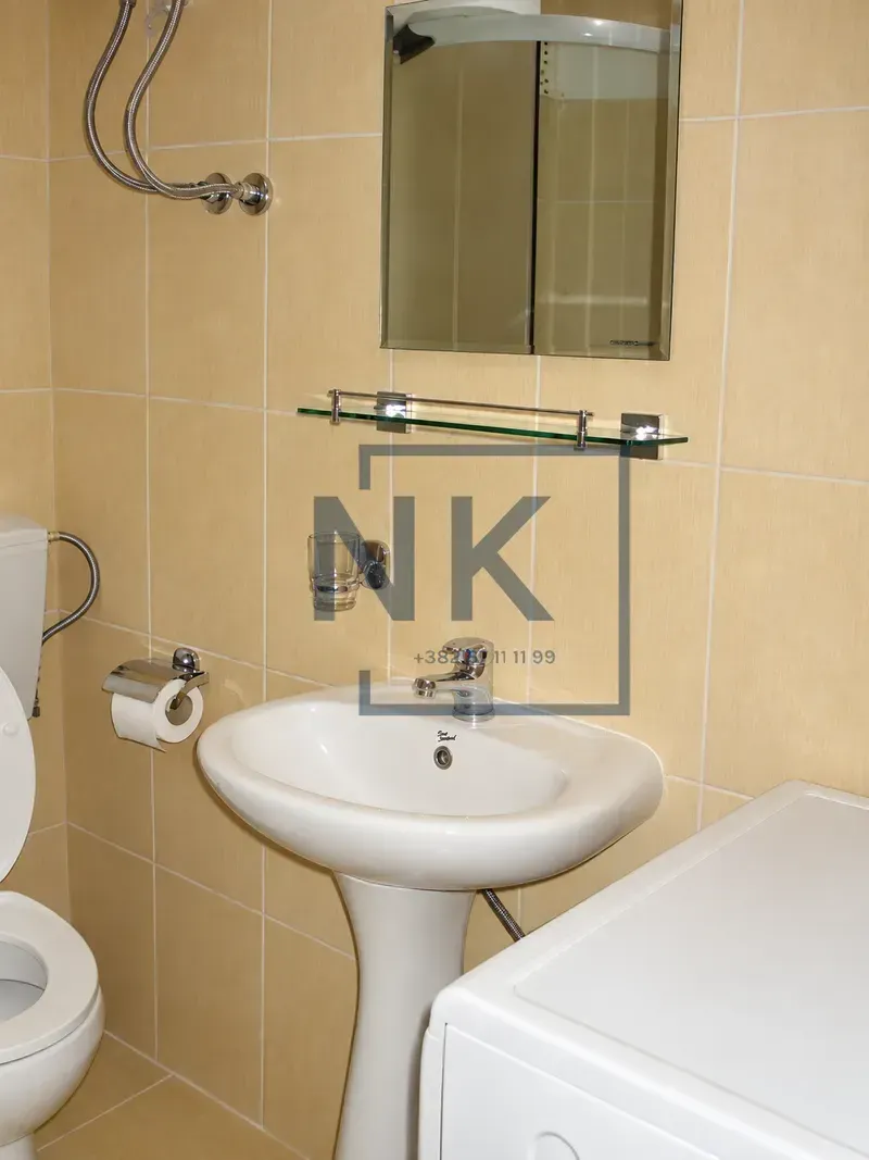 Smaller bathroom with a washbasin, mirror, and toilet bowl tiled with ceramic tiles.