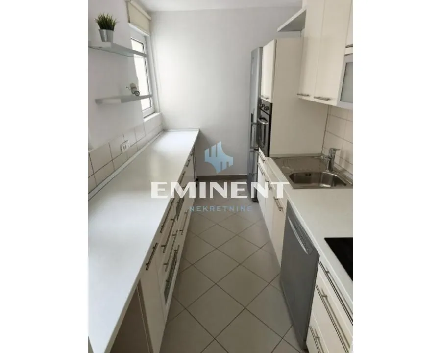 Small narrow kitchen with white units and a window.
