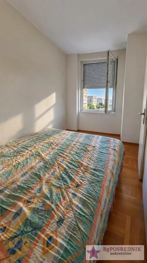 A bedroom with a double bed and a window overlooking surrounding buildings.