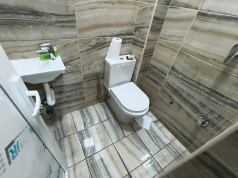 Small bathroom with a toilet, washbasin, and marble-patterned tiles. - image 2