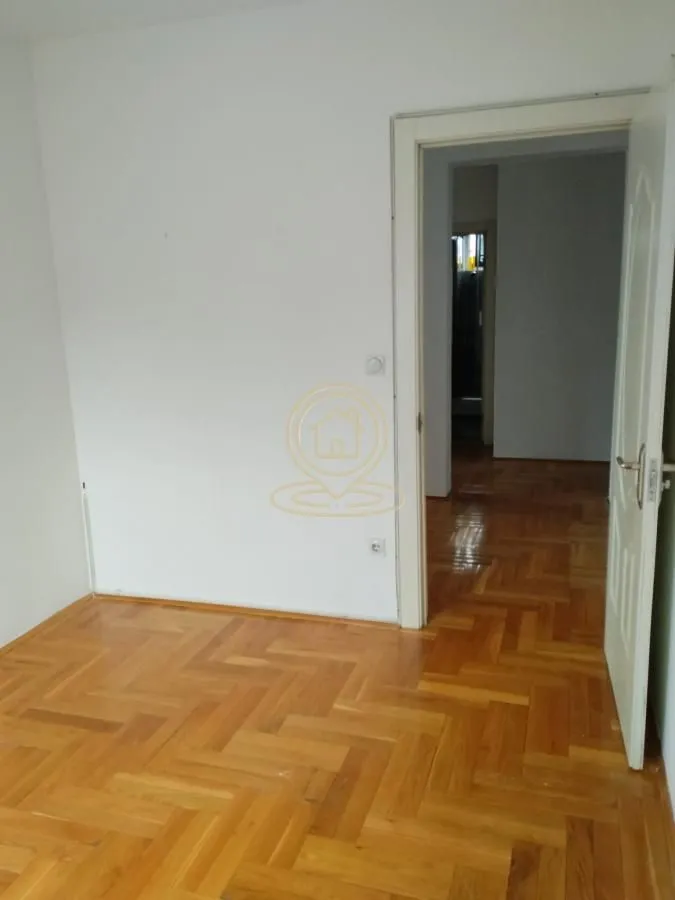 Prazna soba sa parketom i otvorenim vratima prema hodniku.