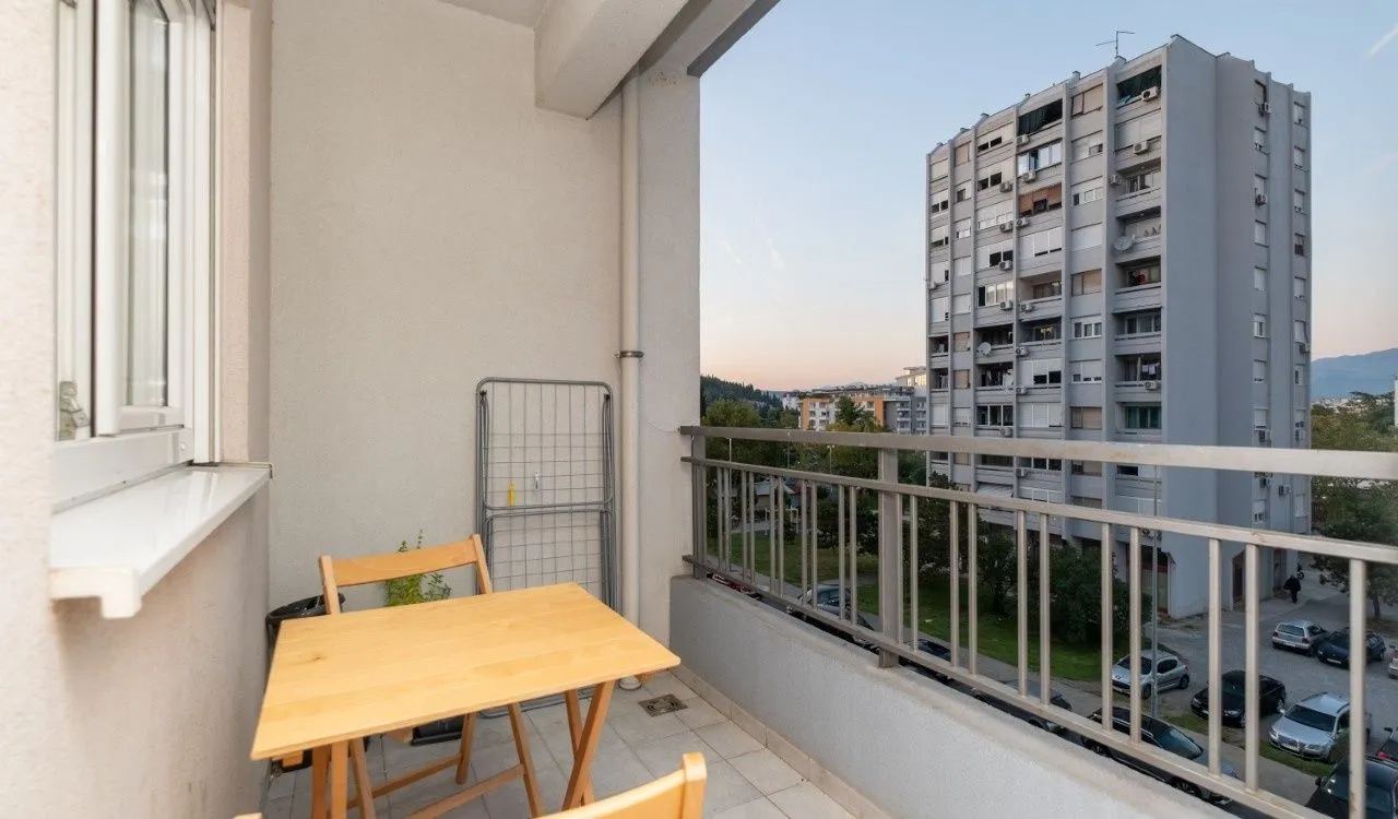 Manji balkon sa drvenim stolom i pogledom na okolne zgrade.