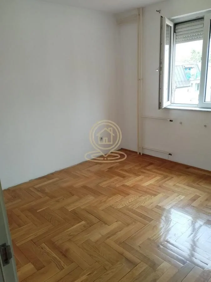 Prazna soba sa parketom i prozorom.