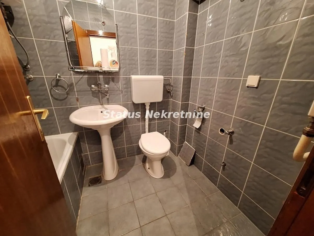 Manje kupatilo obloženo sivim pločicama sa umivaonikom, WC šoljom i kadom.
