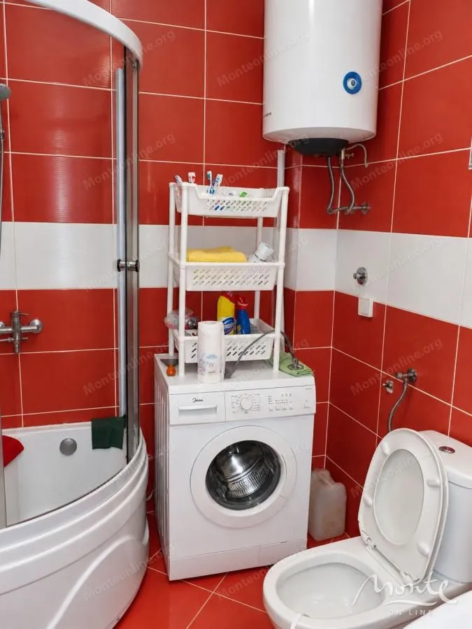 Bathroom with a shower cabin, washing machine, and red tiles.