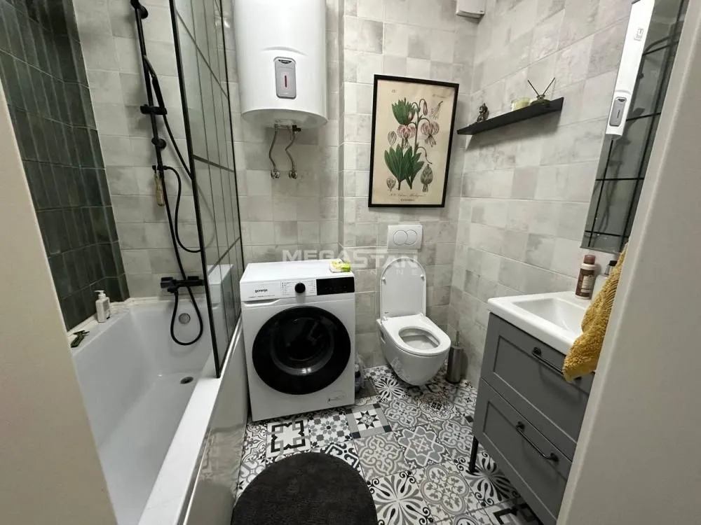 Kompaktno opremljeno kupatilo sa kadom, veš mašinom i WC šoljom.
