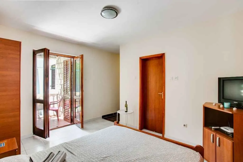 Svijetla spavaća soba sa izlazom na balkon i drvenim namještajem.