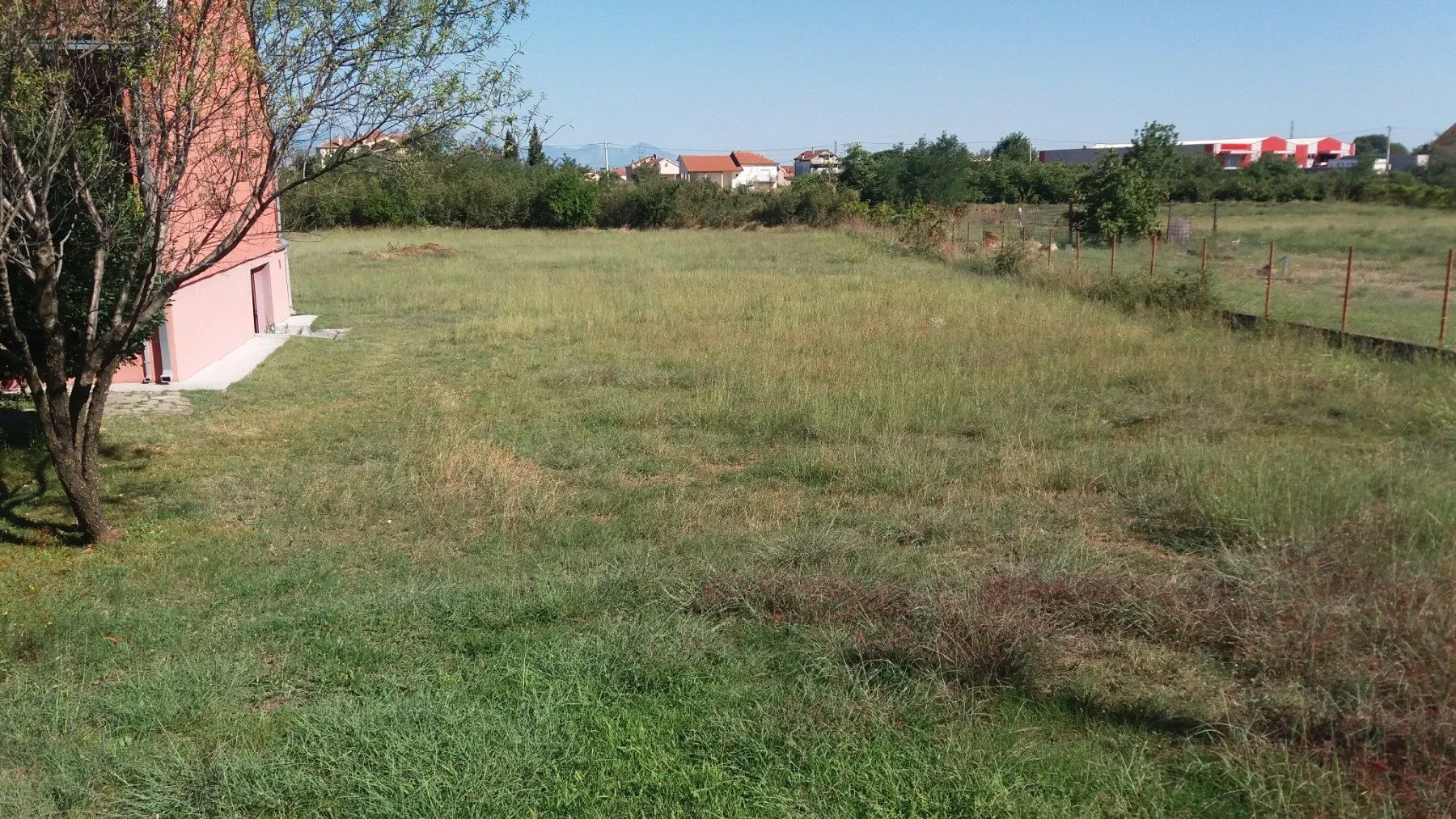 Prostrana travnata parcela pored stambene zgrade.