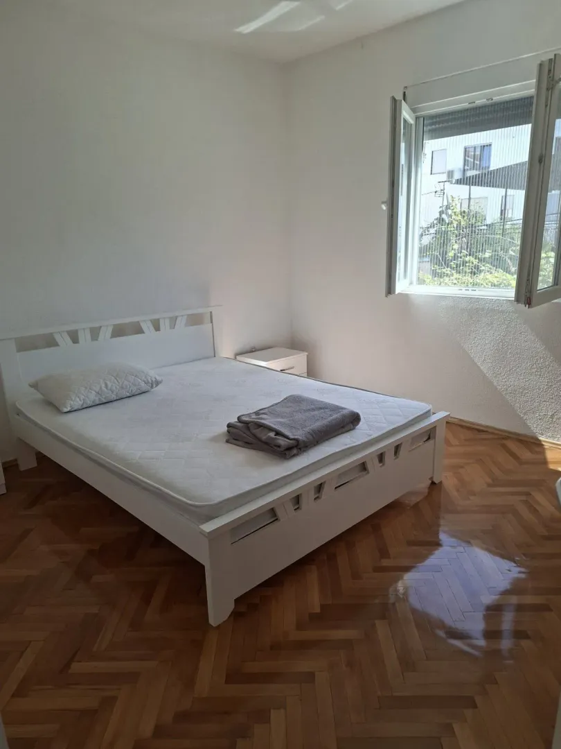 Svijetla spavaća soba sa bijelim bračnim krevetom i drvenim parketom.
