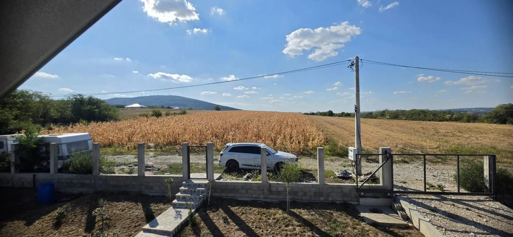 Pogled iz dvorišta na polje i okolni pejzaž sa ograđenim placem.