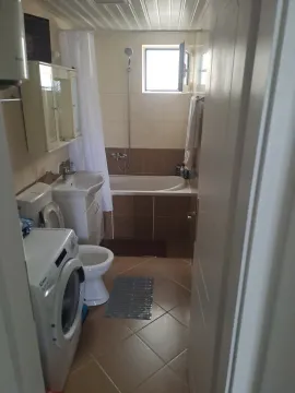 Smaller bathroom with a bathtub, washbasin, toilet, and washing machine. - image 10