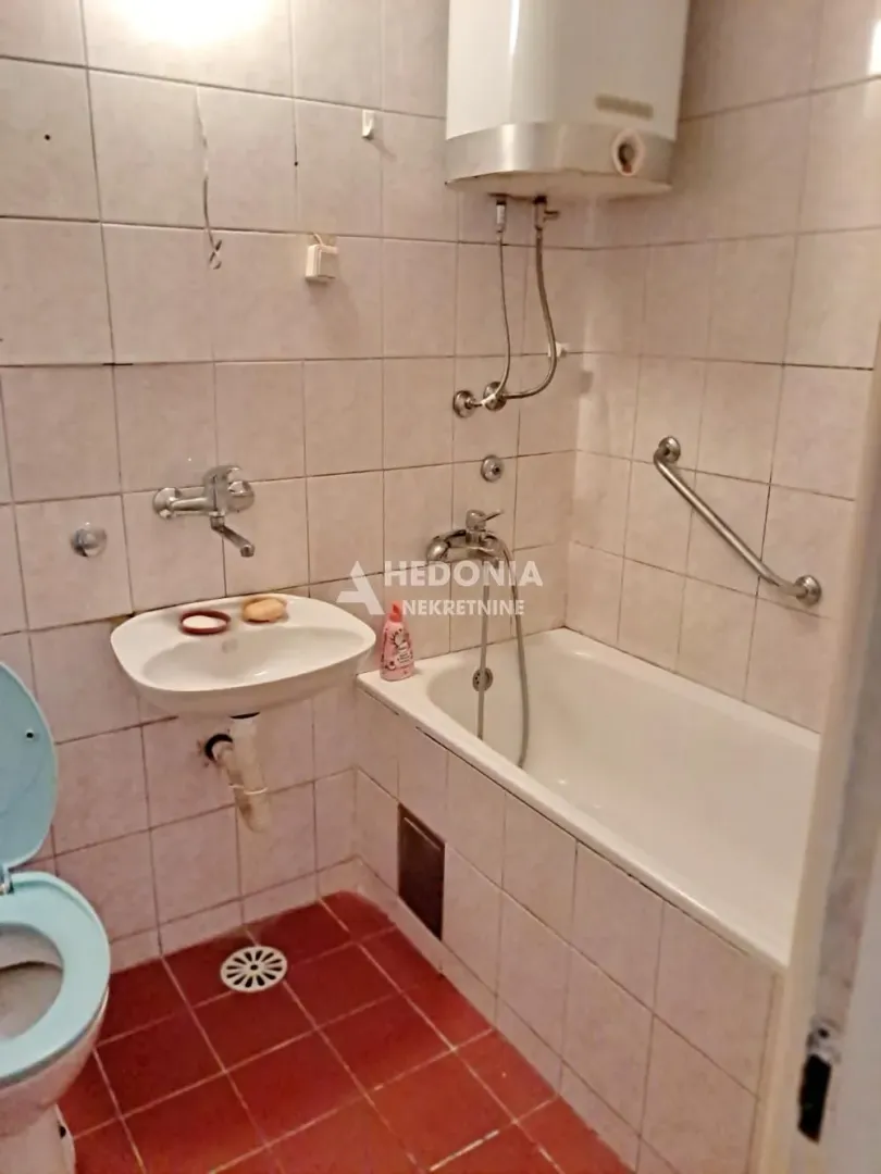 Manje kupatilo sa kadom, umivaonikom i wc šoljom obloženo keramičkim pločicama.
