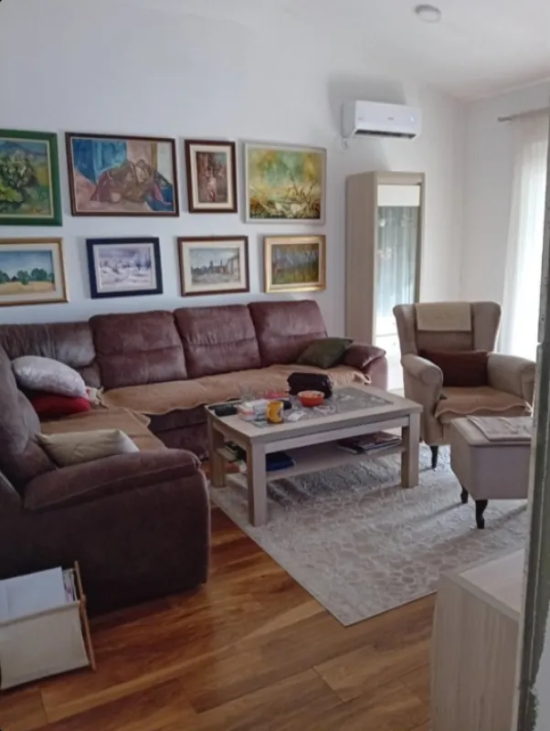Dnevna soba sa garniturom, foteljom i slikama na zidu.