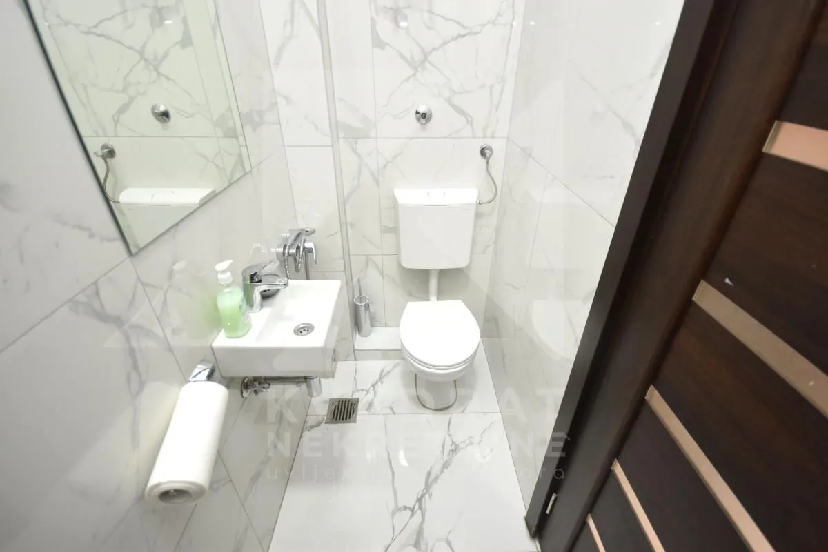Smaller bathroom with white marble tiles, toilet and washbasin.